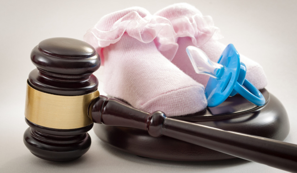 Family law and child custody concept with a blue pacifier and a pair of pink baby shoes next to a judge's gavel